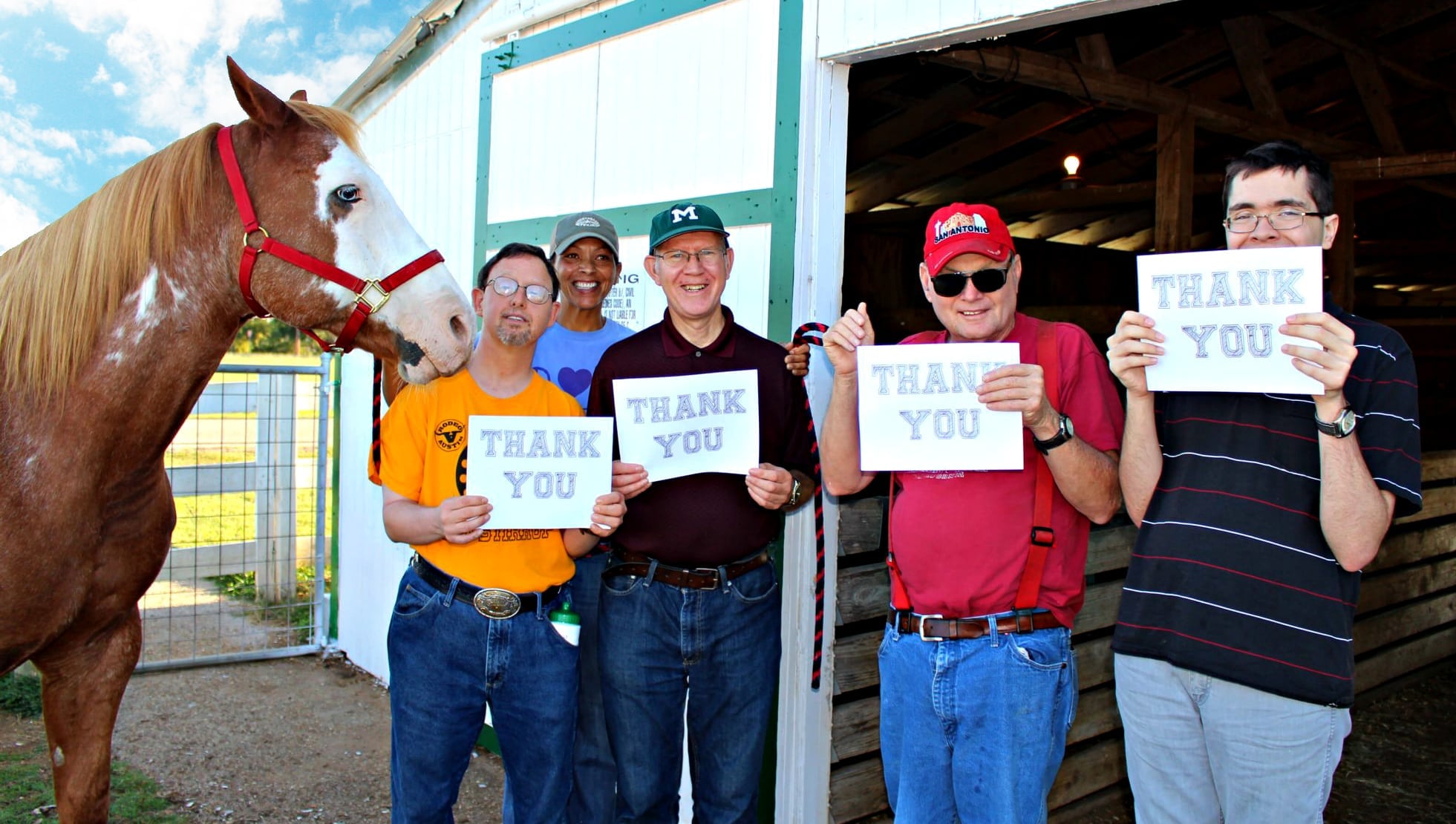 Four residents holding signs that say Thank You stand next to a volunteer and a horse outside of a stable.