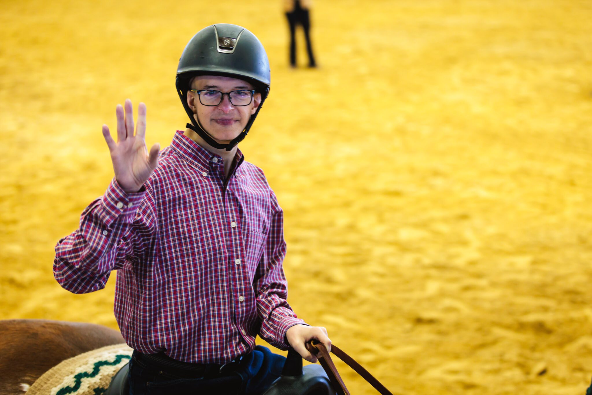 A man waving while riding on the back of a brown horse.