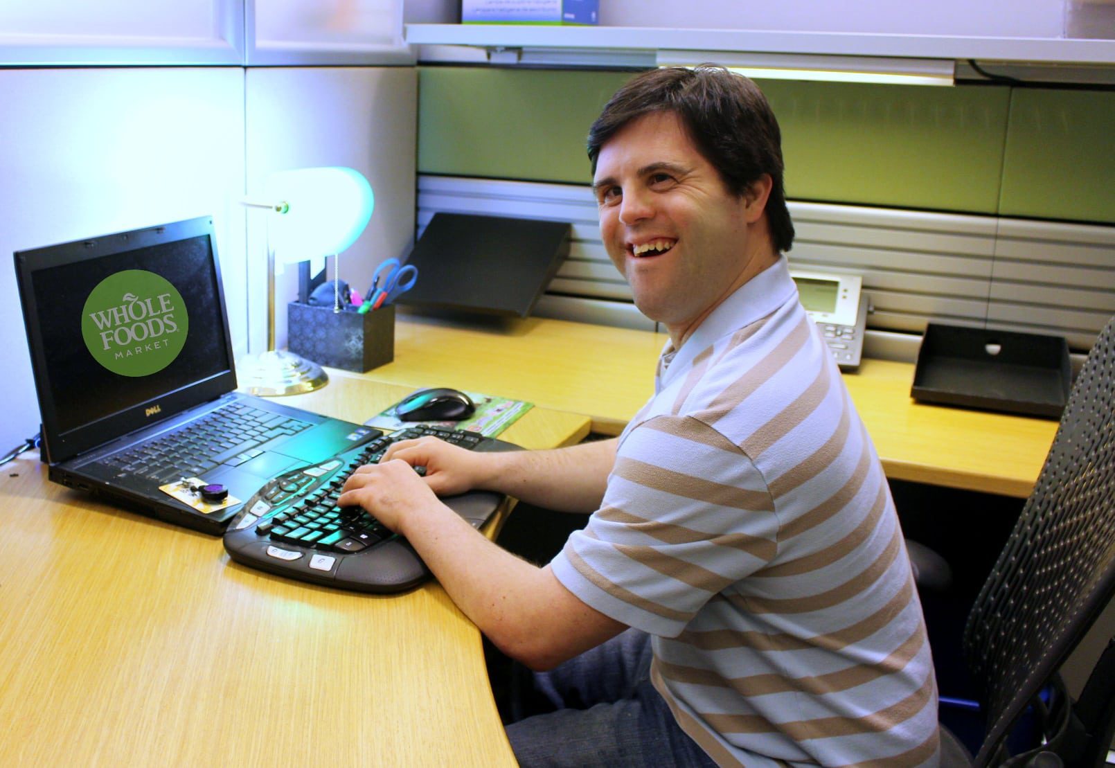 A smiling young resident is seated at a desk typing on a laptop computer.