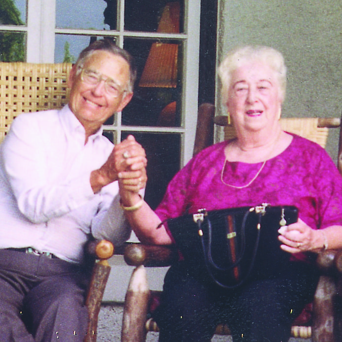 Ed and Marge Bridges smile and hold hands while sitting on a porch at Marbridge.