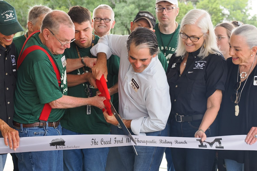 People gather as two men ceremoniously cut a ribbon at the opening of The Creed Ford III Therapeutic Riding Ranch.