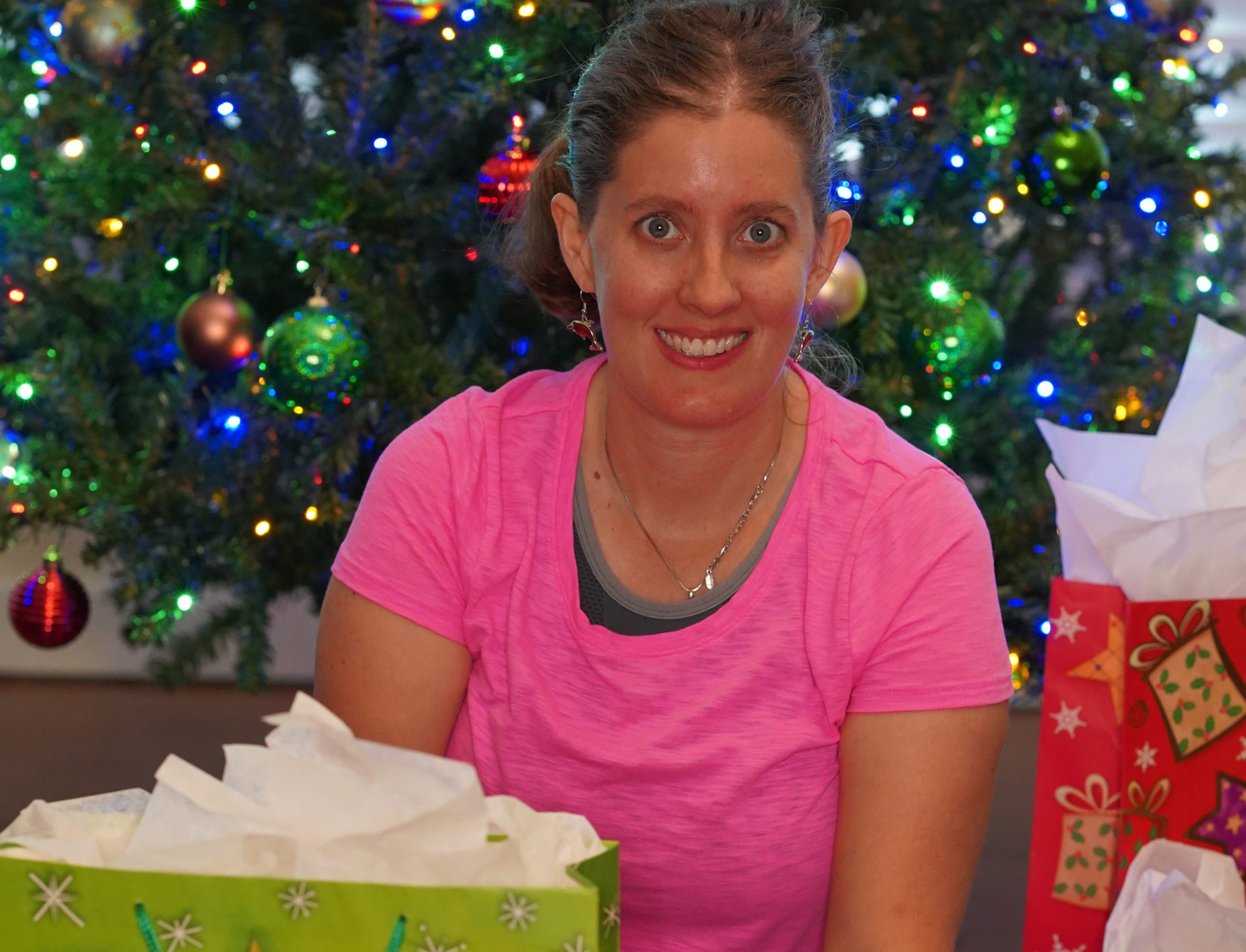A woman sitting in front of a Christmas tree surrounded by presents.