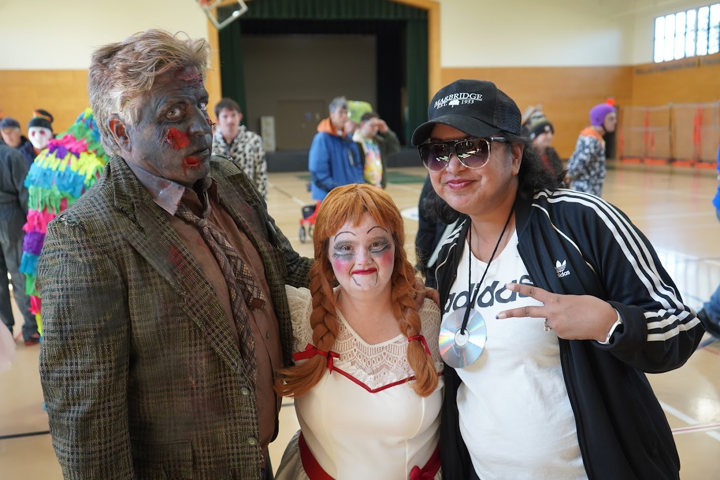 Three people in Halloween costumes: one dressed as a zombie, one as a doll with pigtails, and one dressed as a rapper.