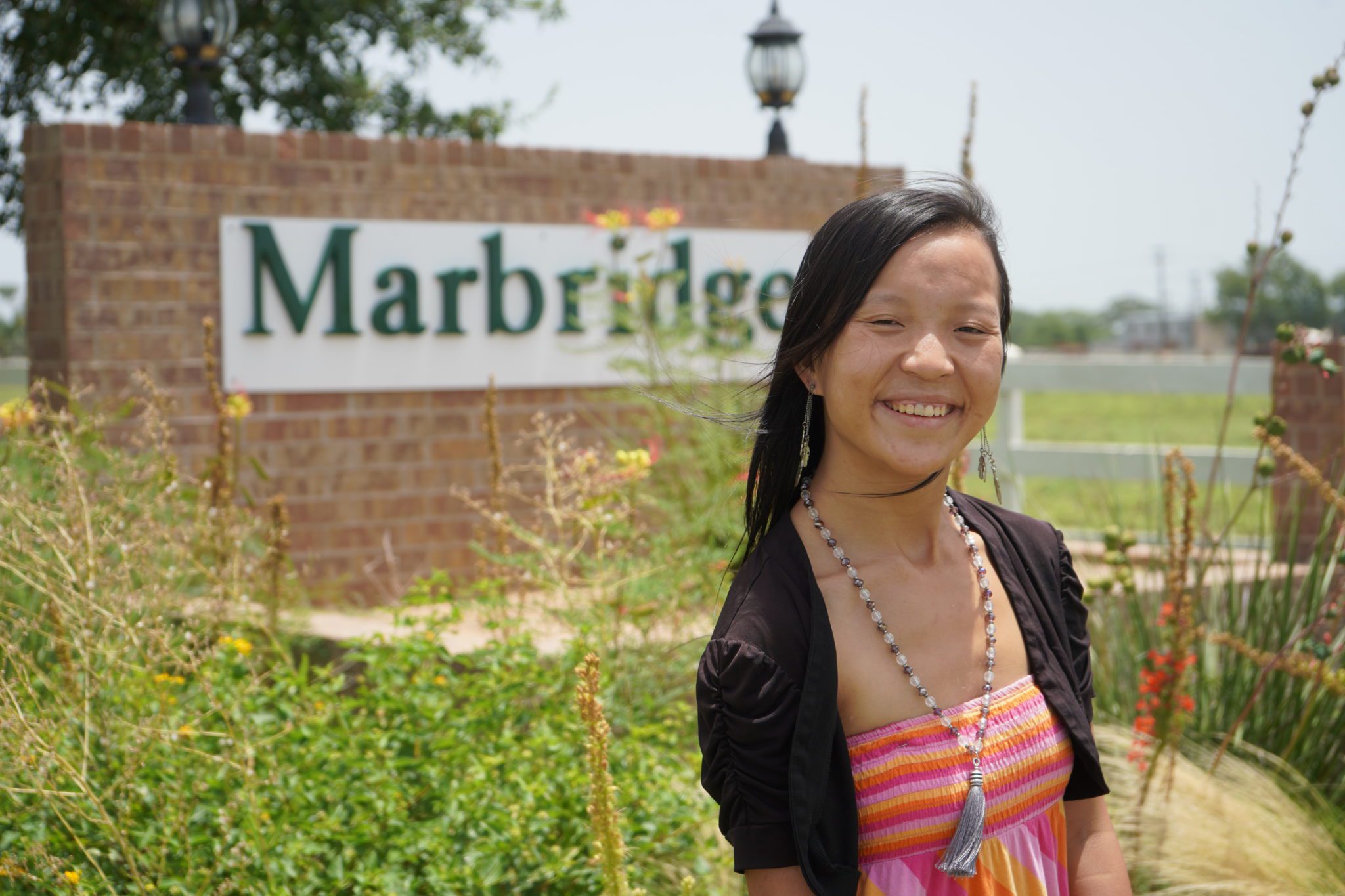 A woman smiling in front of the Marbridge entrance sign.