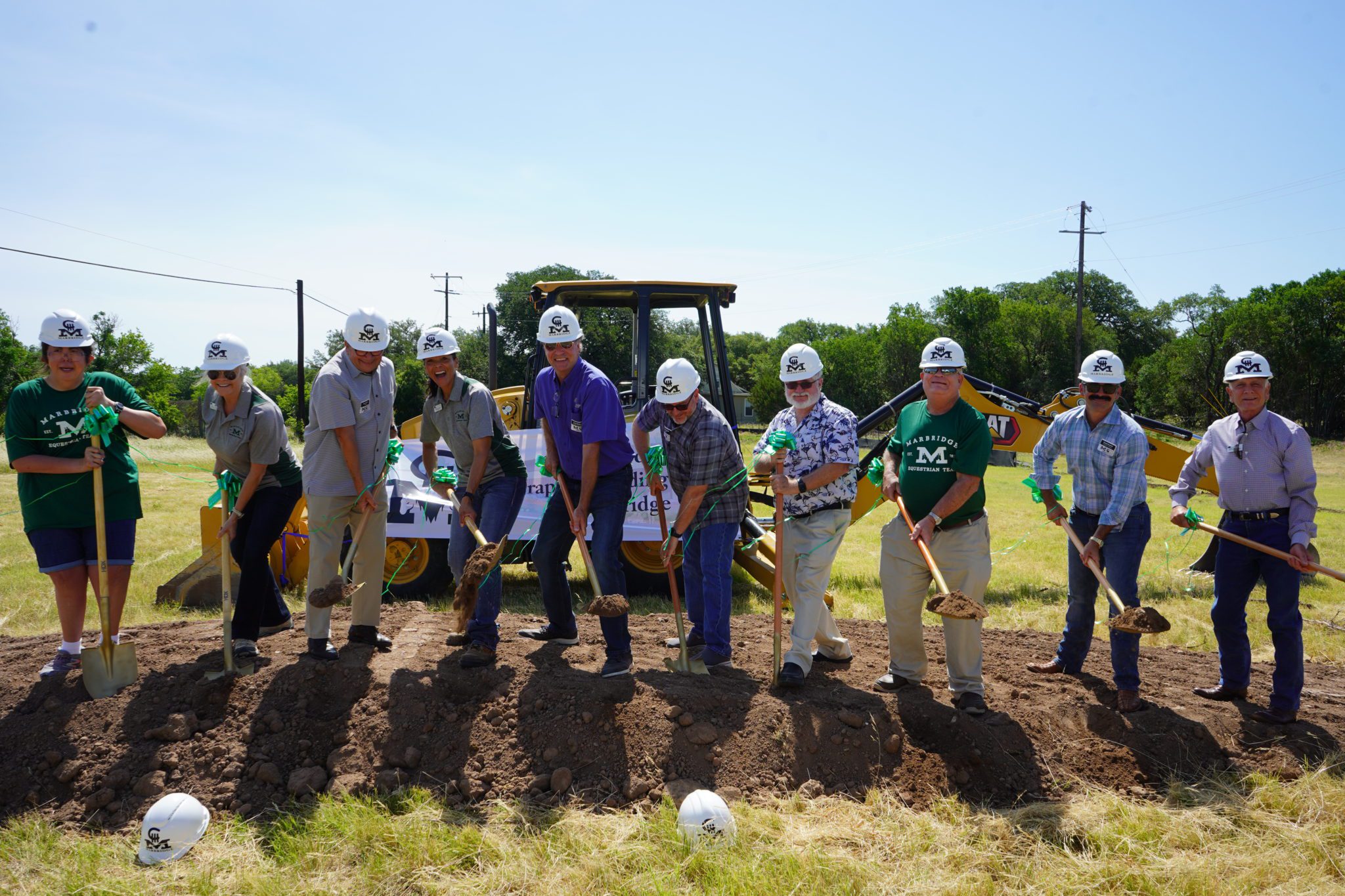 A group of people wearing hard hats and holding shovels participate in the C3 Riding Ranch groundbreaking ceremony.