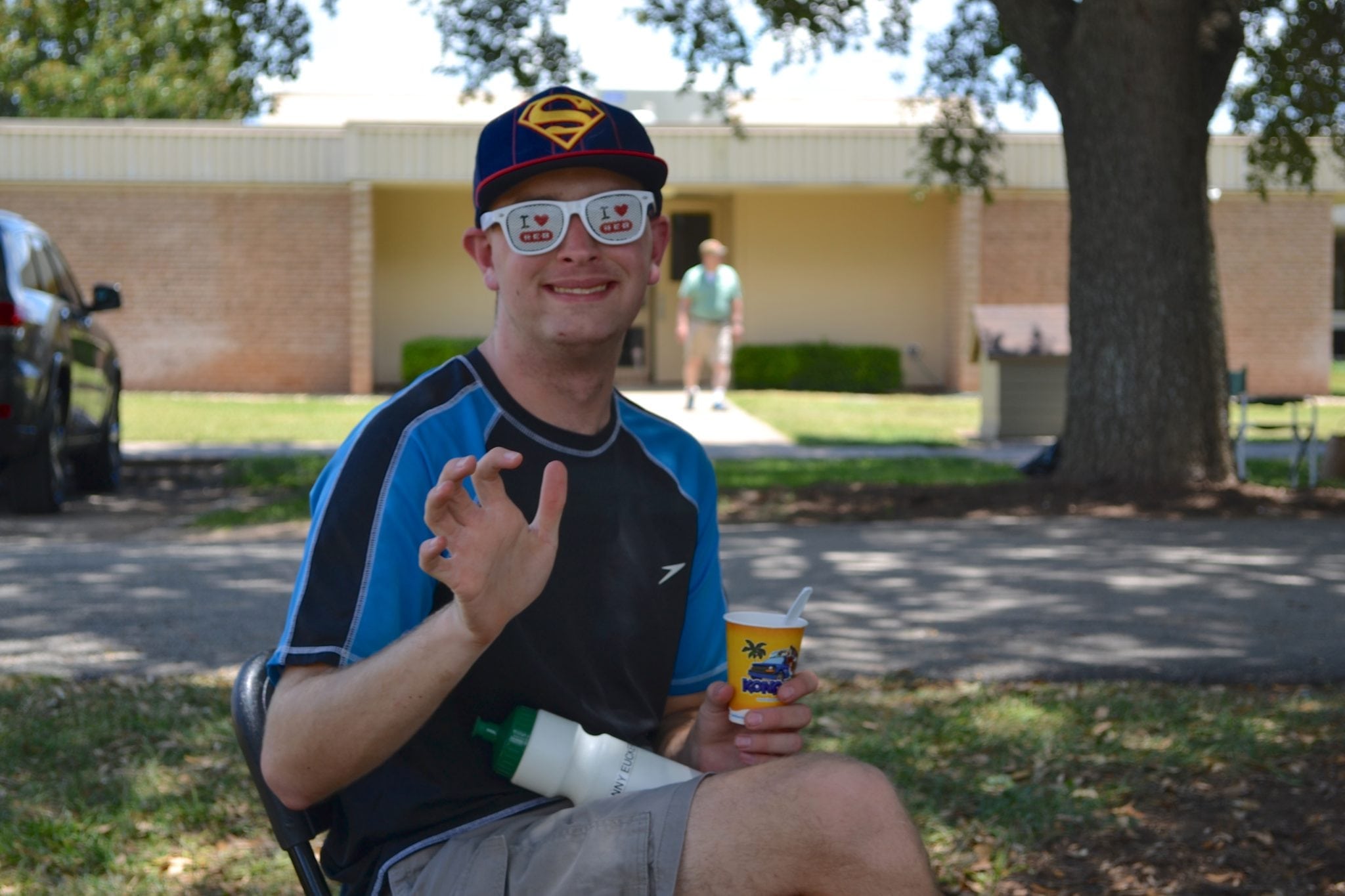 A smiling man wearing sunglasses sitting in a chair holding a cup of ice cream.