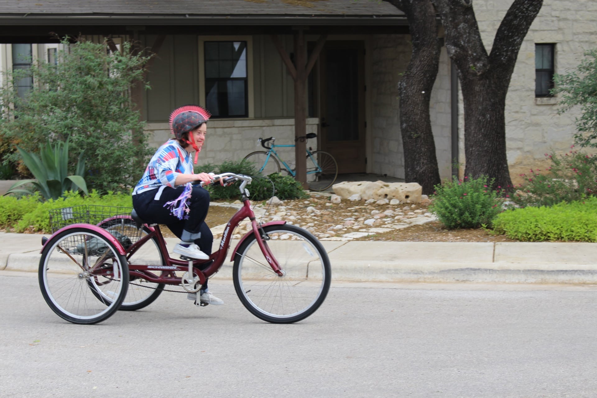 A young female resident wearing a helmet pedals an adult tricycle on the Marbridge campus.