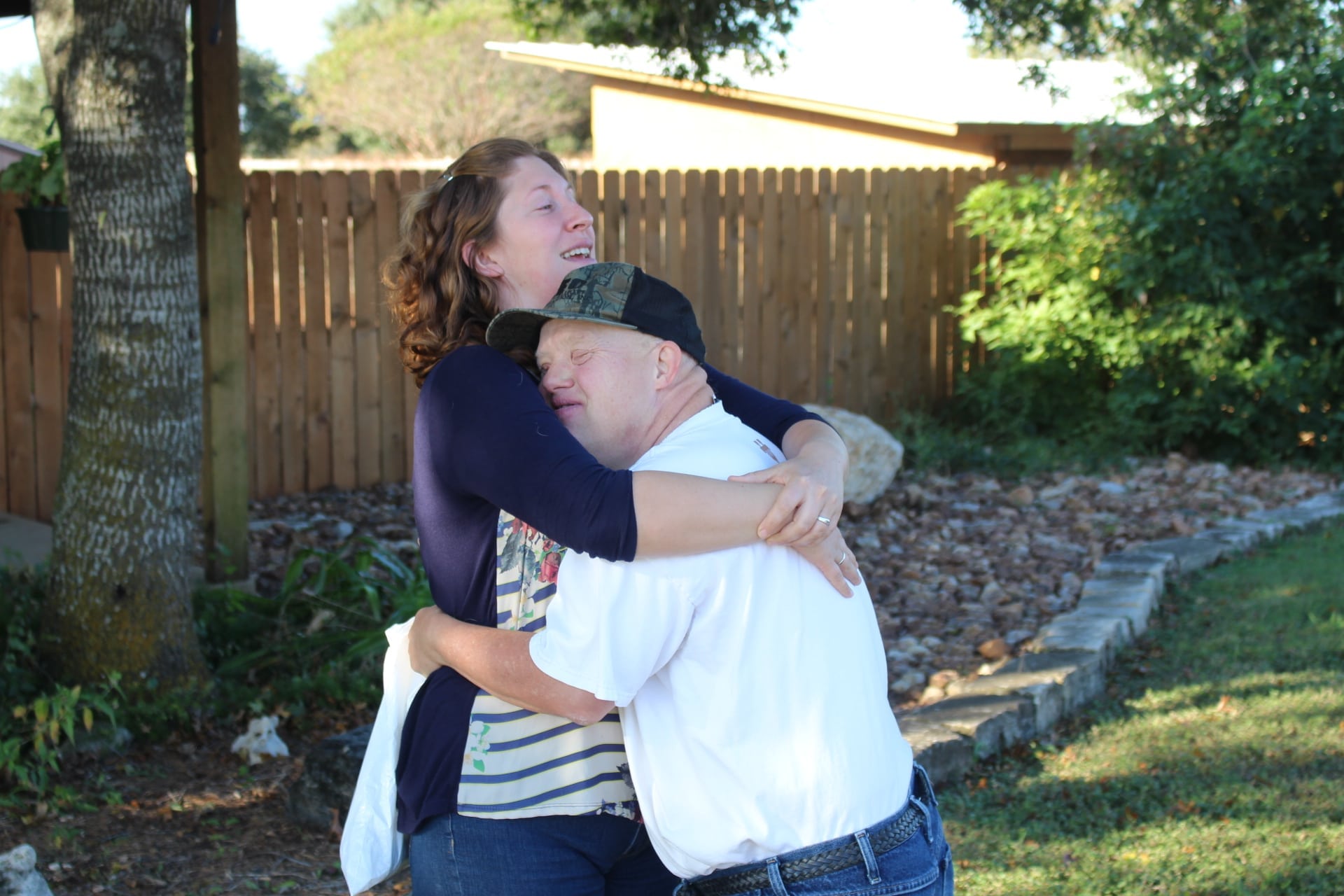 A woman hugging a man wearing a baseball cap.