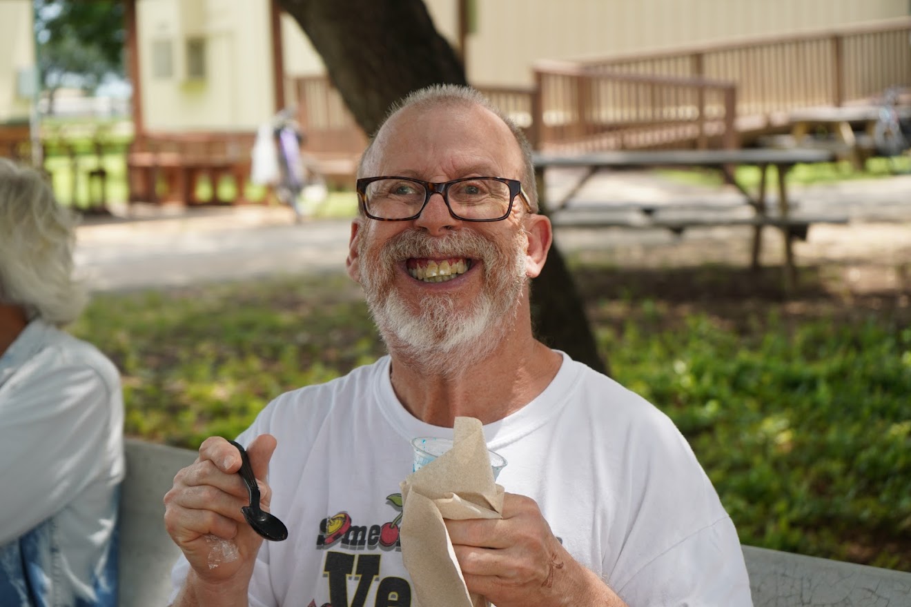 A smiling man with a white beard and glasses holding a spoon and napkin.