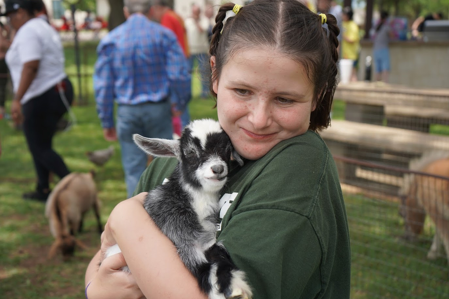 A girl with braided hair and a green shirt smiles while holding a small black and white baby goat at the 2022 Ranch Round Up.