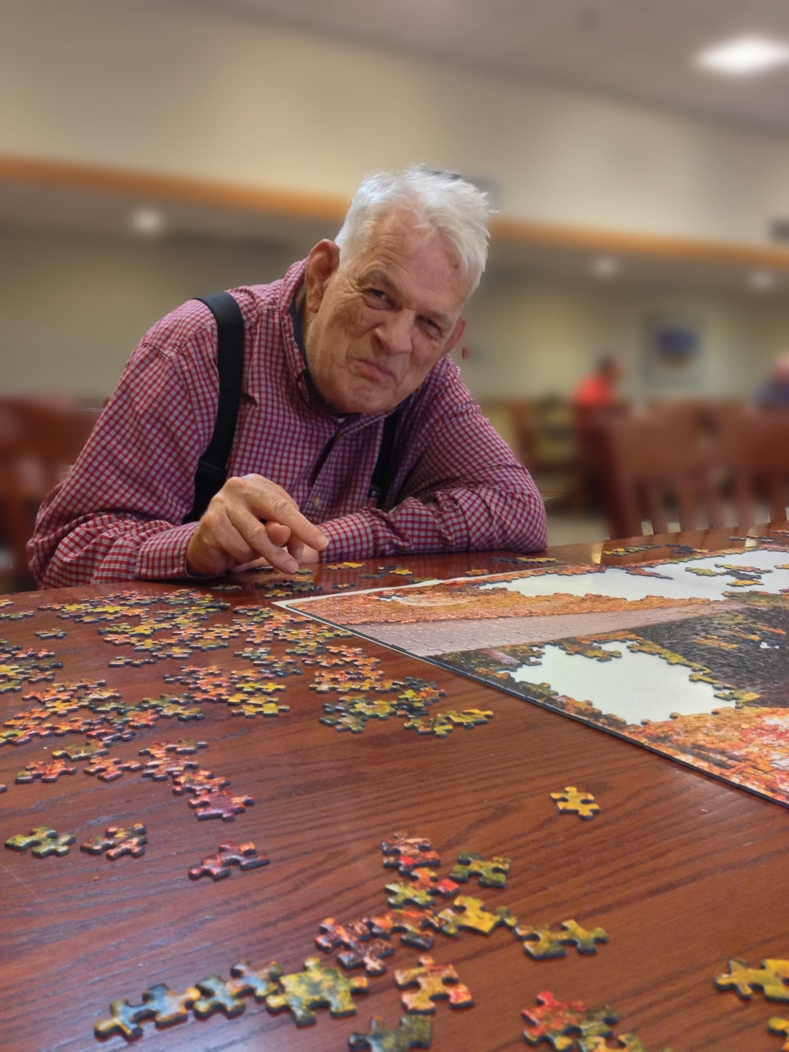 A smiling man sitting at a table working on a jigsaw puzzle.