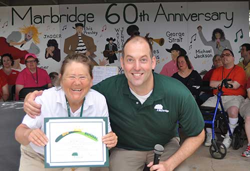 A man and a woman holding an award posing for a picture at the Marbridge 60th Anniversary.