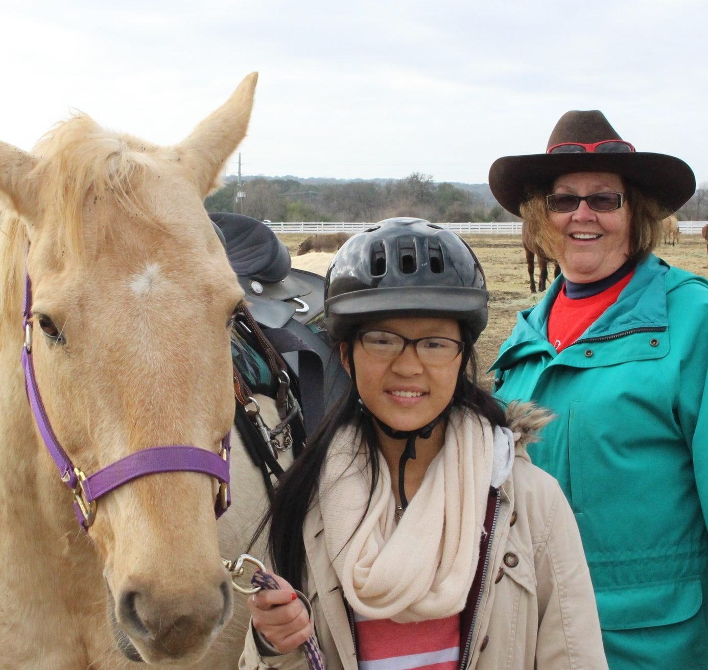 A young woman holding on to a horse's bridle while standing next to her volunteer riding instructor.